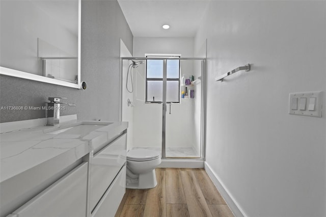 bathroom featuring wood-type flooring, toilet, a shower with shower door, and vanity