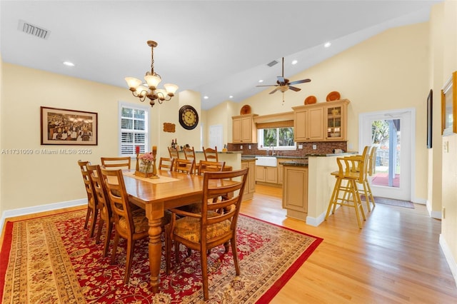 dining space featuring sink, ceiling fan with notable chandelier, high vaulted ceiling, and light hardwood / wood-style flooring