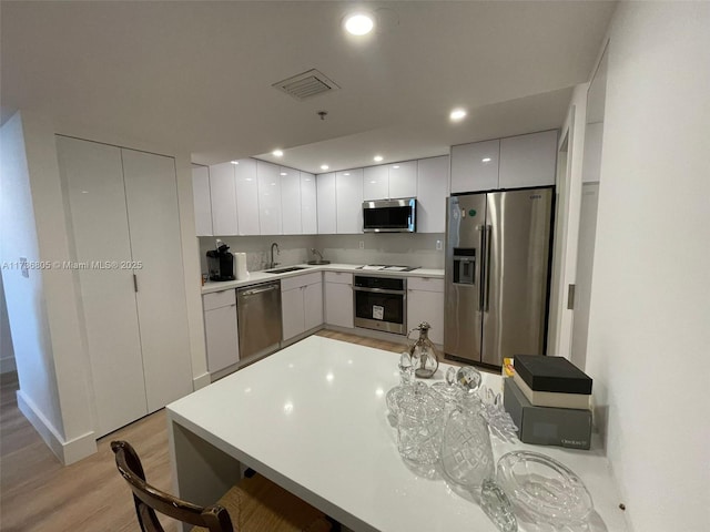 kitchen with white cabinetry, stainless steel appliances, light hardwood / wood-style floors, and sink