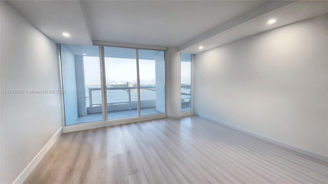 spare room featuring recessed lighting, a water view, baseboards, light wood-type flooring, and floor to ceiling windows