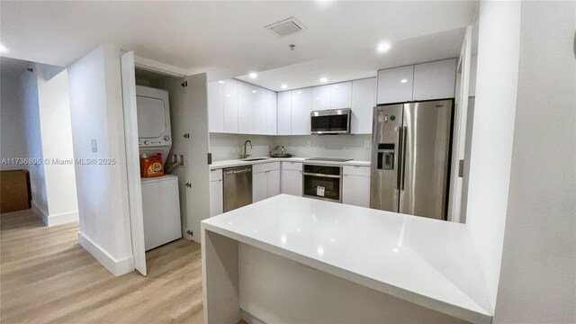 kitchen featuring stainless steel appliances, stacked washer / drying machine, light countertops, white cabinetry, and modern cabinets