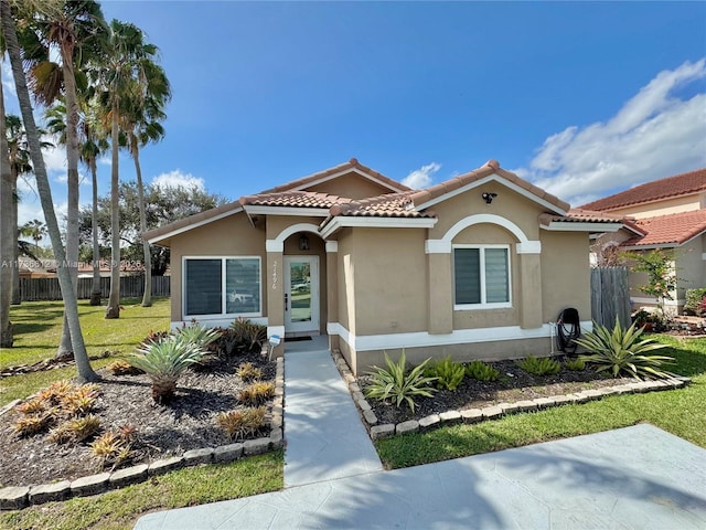 mediterranean / spanish-style home with a front yard, fence, a tile roof, and stucco siding