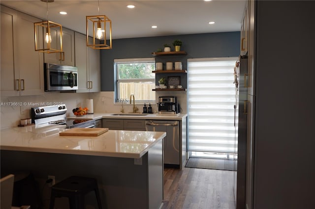 kitchen with pendant lighting, open shelves, appliances with stainless steel finishes, a sink, and a peninsula