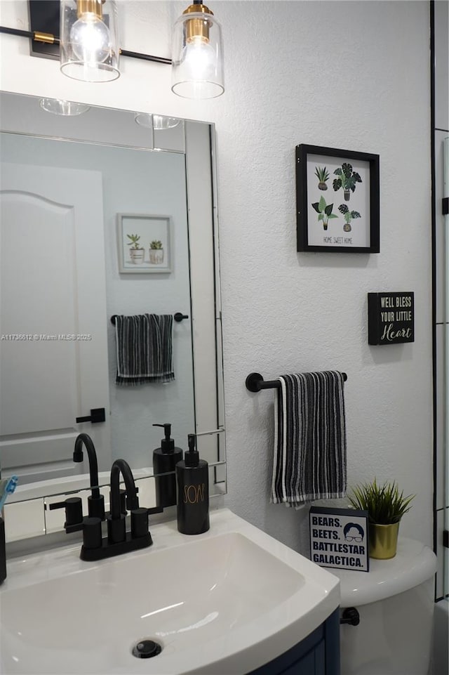 bathroom with toilet, a textured wall, and vanity