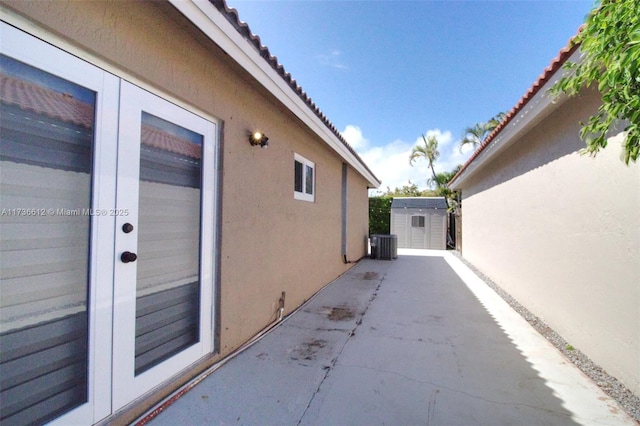 view of property exterior featuring an outbuilding, central AC, stucco siding, a shed, and a patio area