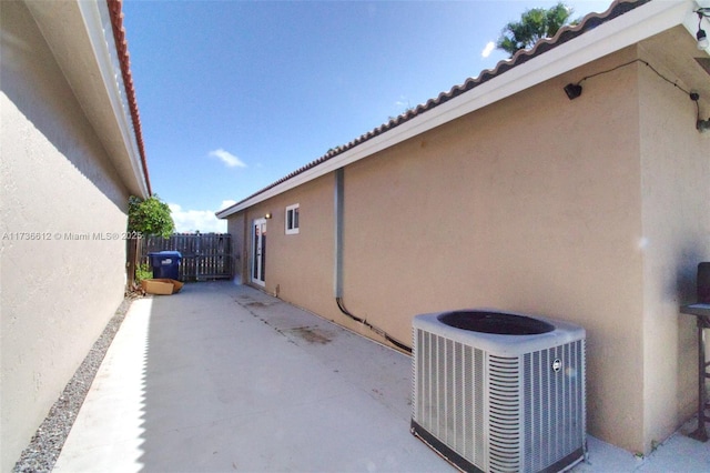 view of side of home with a patio area, stucco siding, fence, and central air condition unit