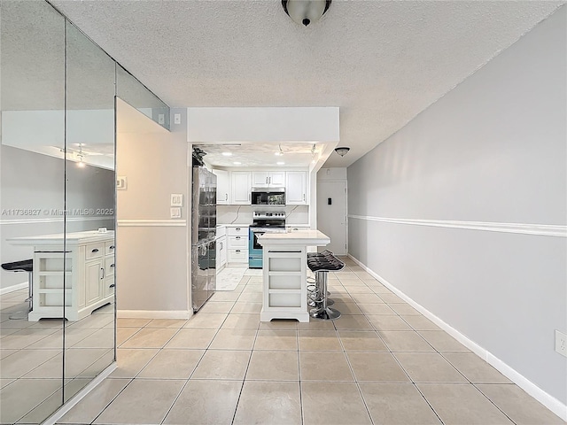 interior space with a kitchen bar, white cabinetry, light tile patterned floors, appliances with stainless steel finishes, and a kitchen island