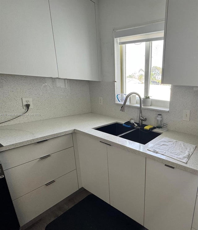 kitchen featuring light stone countertops, sink, white cabinets, and decorative backsplash