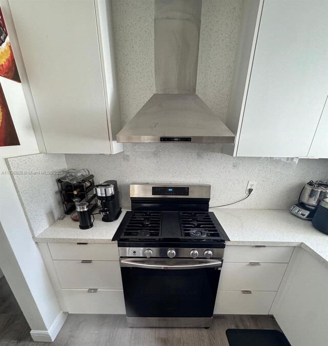 kitchen featuring white cabinetry, wall chimney range hood, backsplash, and gas stove