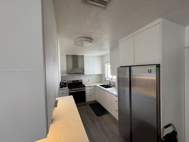 kitchen featuring dark hardwood / wood-style floors, white cabinetry, sink, stainless steel appliances, and wall chimney range hood