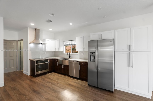 kitchen with white cabinetry, sink, stainless steel appliances, dark wood-type flooring, and wall chimney range hood