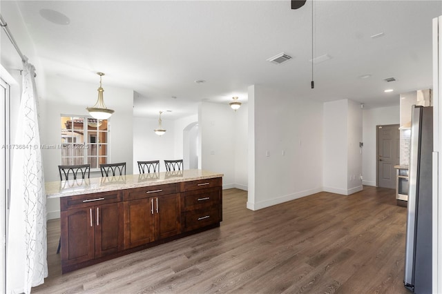 kitchen with hanging light fixtures, stainless steel fridge, a kitchen breakfast bar, and wood-type flooring