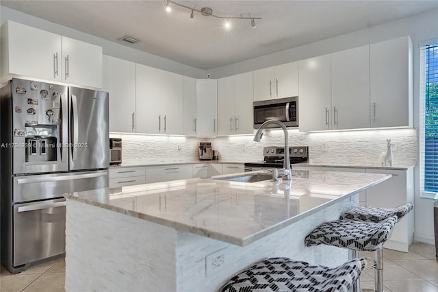 kitchen featuring light stone countertops, an island with sink, appliances with stainless steel finishes, and white cabinets