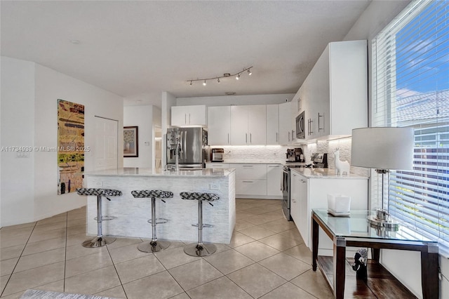 kitchen with light tile patterned flooring, a breakfast bar, white cabinetry, stainless steel appliances, and backsplash