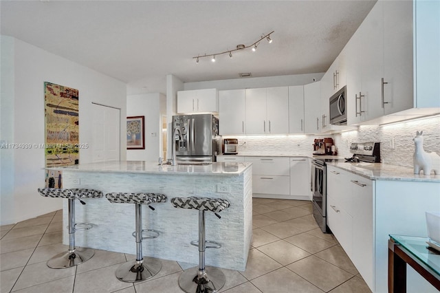 kitchen with appliances with stainless steel finishes, white cabinetry, backsplash, a kitchen bar, and light tile patterned floors