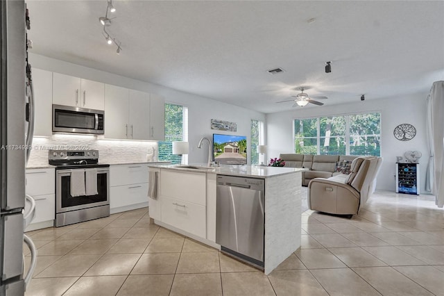 kitchen with appliances with stainless steel finishes, a kitchen island with sink, sink, and white cabinets