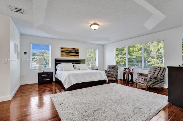 bedroom with multiple windows, dark wood-type flooring, a textured ceiling, and a tray ceiling