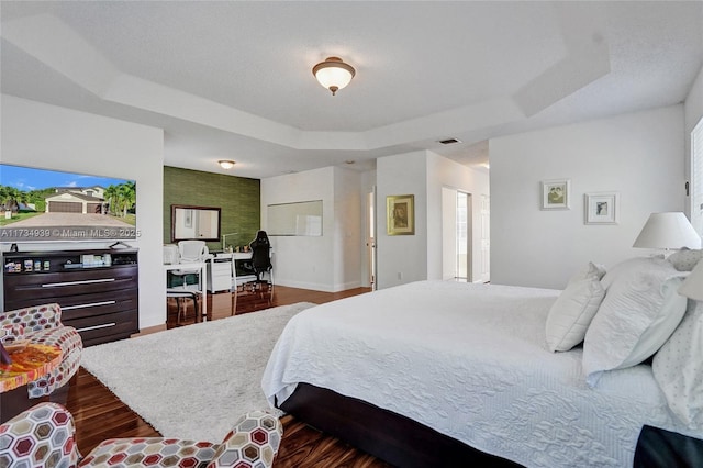 bedroom featuring hardwood / wood-style floors, a tray ceiling, and a textured ceiling