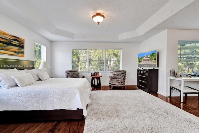 bedroom with dark wood-type flooring, a tray ceiling, and a textured ceiling