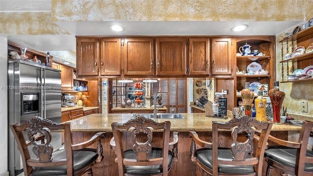 kitchen featuring high end refrigerator, light stone counters, a kitchen breakfast bar, and kitchen peninsula