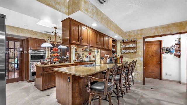 kitchen featuring a breakfast bar area, hanging light fixtures, double oven, light stone counters, and kitchen peninsula