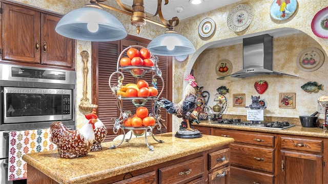 kitchen with light stone countertops, appliances with stainless steel finishes, and wall chimney range hood