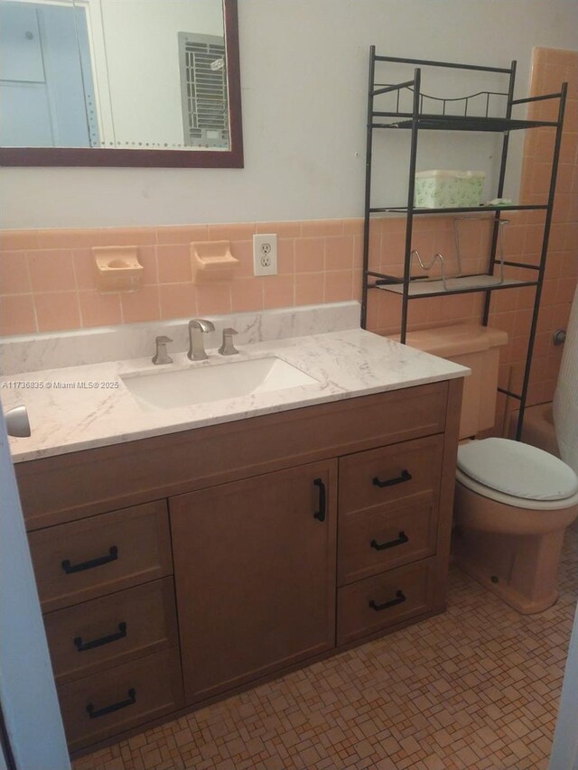 bathroom with vanity, toilet, and tile walls