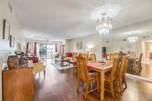 dining space with a textured ceiling, ceiling fan with notable chandelier, wood finished floors, and visible vents