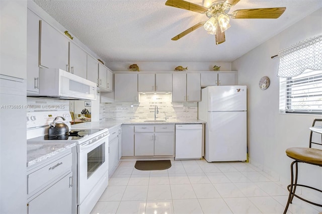 kitchen featuring white appliances, decorative backsplash, light countertops, a textured ceiling, and a sink