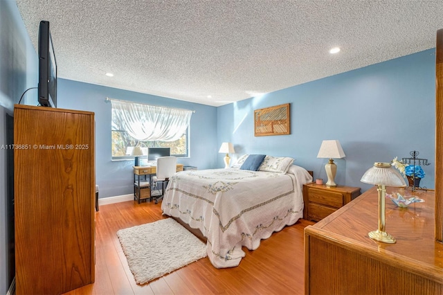 bedroom featuring baseboards, a textured ceiling, and light wood finished floors