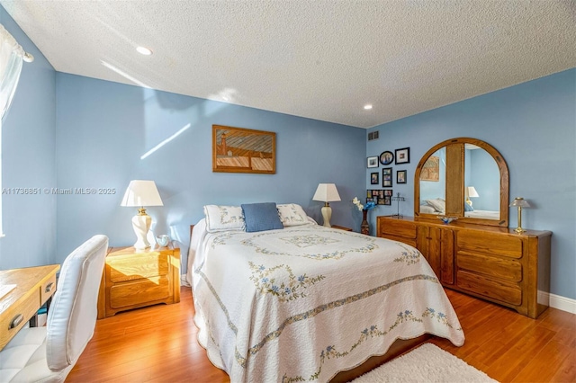 bedroom with light wood-type flooring, visible vents, a textured ceiling, and baseboards