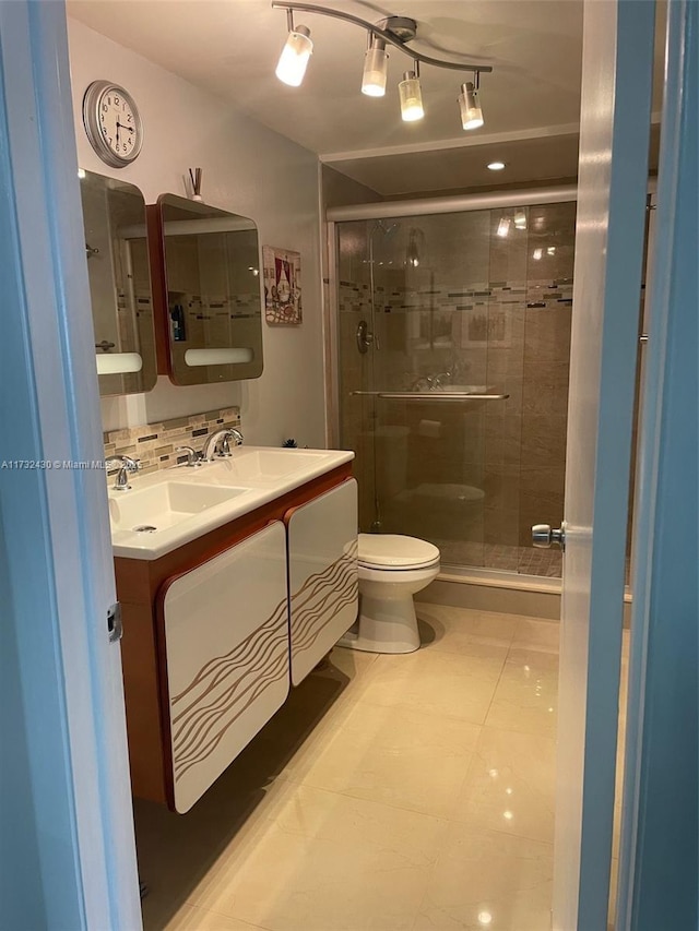 bathroom featuring toilet, vanity, a shower with door, tile patterned flooring, and backsplash