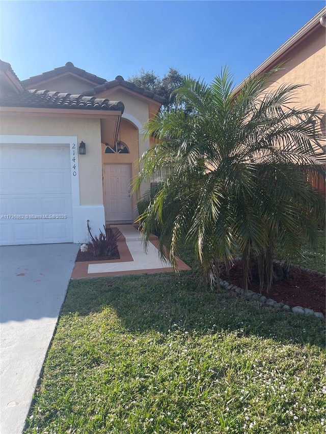 doorway to property featuring a lawn, an attached garage, a tile roof, and stucco siding