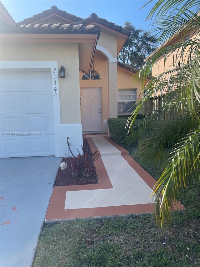 view of exterior entry with a garage, a tiled roof, and stucco siding