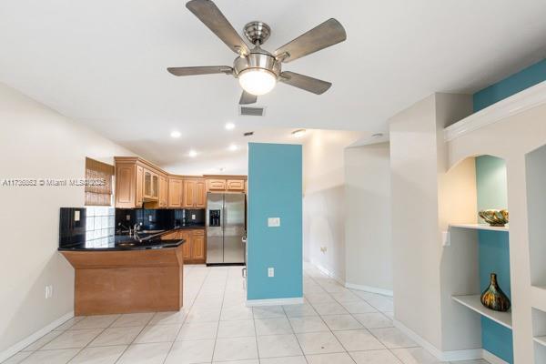 kitchen with sink, stainless steel fridge with ice dispenser, light tile patterned floors, kitchen peninsula, and decorative backsplash