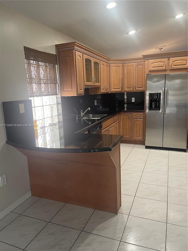 kitchen featuring light tile patterned floors, decorative backsplash, glass insert cabinets, a sink, and stainless steel fridge