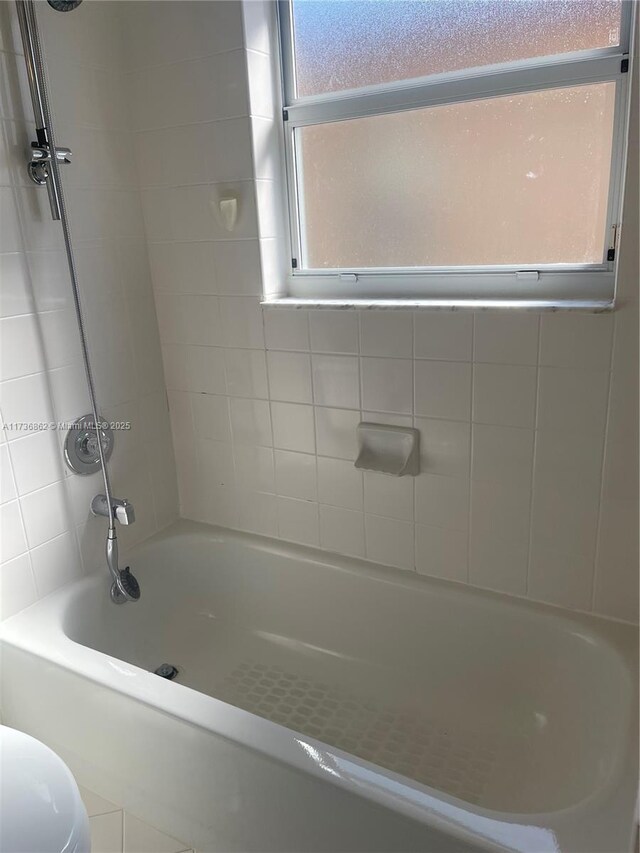 bathroom with tiled shower / bath, a healthy amount of sunlight, and toilet