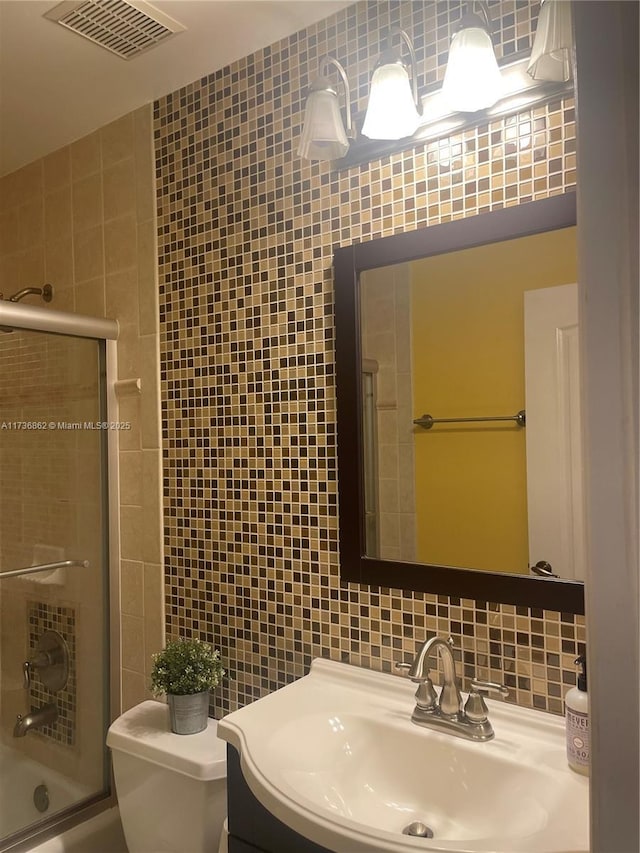 full bathroom with shower / bath combination with glass door, tile walls, vanity, tasteful backsplash, and toilet