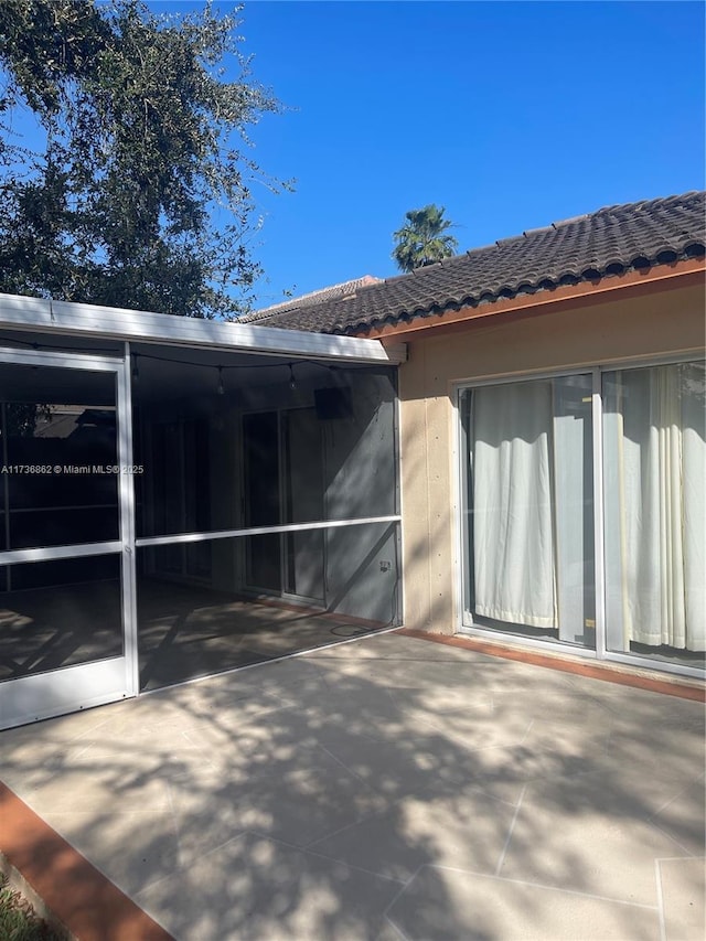 view of side of property featuring a sunroom, a tile roof, an attached carport, and a patio