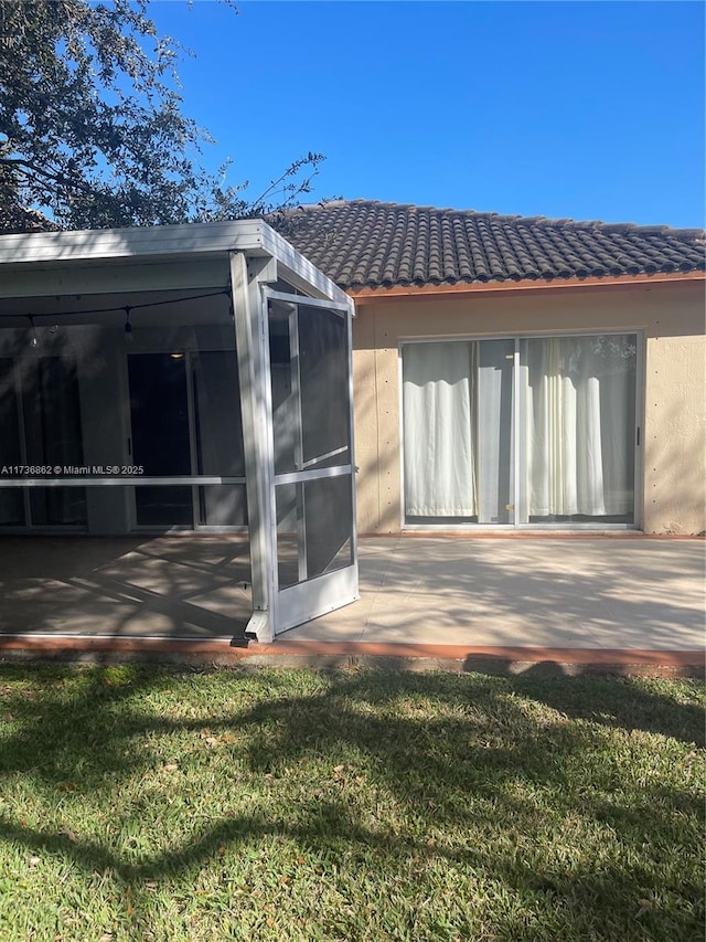 back of house with a sunroom, a tile roof, a lawn, and a patio