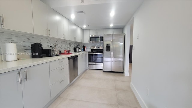 kitchen with light tile patterned flooring, sink, tasteful backsplash, stainless steel appliances, and white cabinets