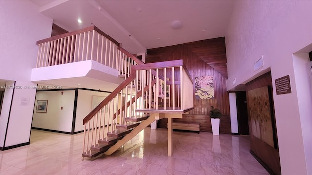 staircase with a towering ceiling and wood walls