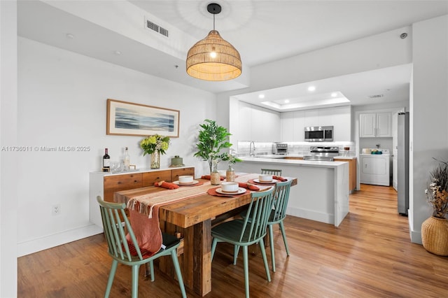 dining space with washer / clothes dryer, a raised ceiling, sink, and light wood-type flooring