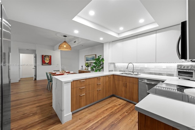 kitchen featuring decorative light fixtures, sink, white cabinets, kitchen peninsula, and a raised ceiling