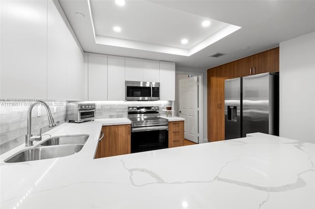 kitchen with a raised ceiling, white cabinetry, sink, backsplash, and stainless steel appliances