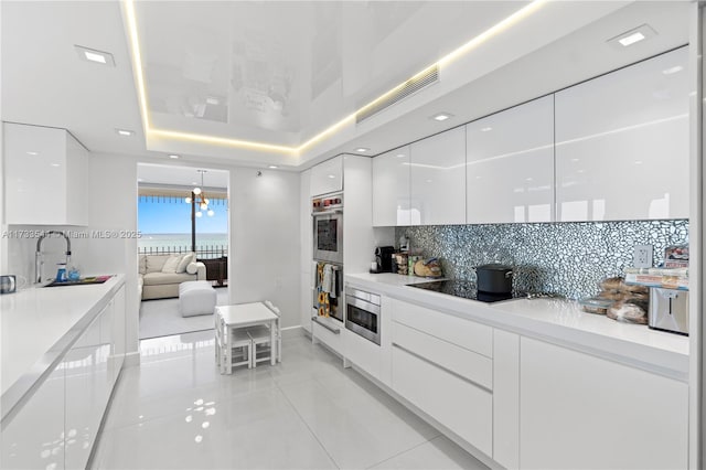 kitchen featuring sink, appliances with stainless steel finishes, white cabinetry, tasteful backsplash, and a tray ceiling