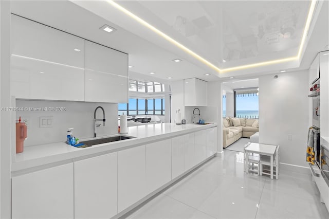 kitchen with sink, light tile patterned floors, white cabinetry, a tray ceiling, and oven