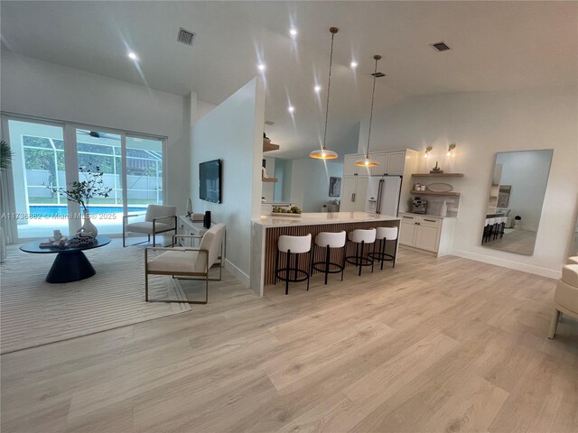 kitchen with a kitchen bar, decorative light fixtures, high vaulted ceiling, light hardwood / wood-style flooring, and white cabinets