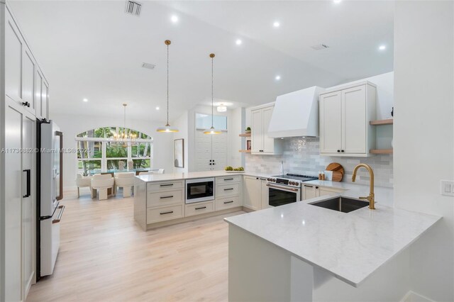 kitchen with sink, custom range hood, built in microwave, decorative light fixtures, and kitchen peninsula