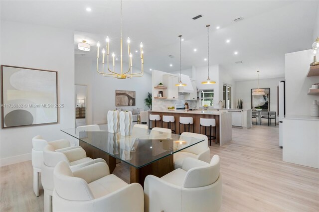 dining room with a notable chandelier, high vaulted ceiling, sink, and light wood-type flooring